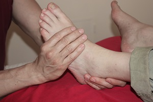 Massagehände halten linken Fuß zur Fußreflexzonenmassage