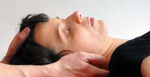 Oberkörper einer liegenden Frau mit zwei Männerhänden zur Nackenmassage